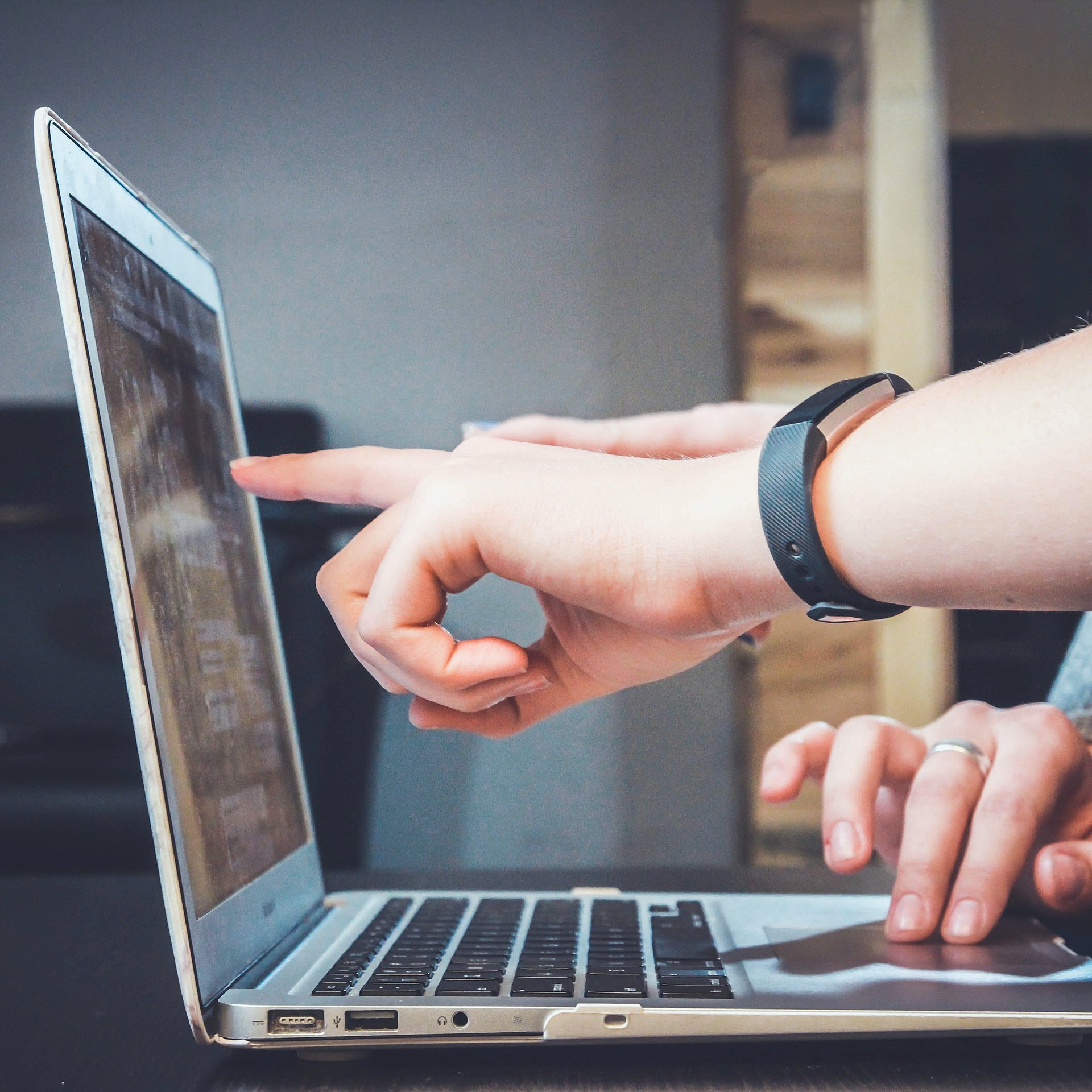 Foto einer Hand, die auf den Bildschirm eines Laptops zeigt. Die andere Hand bedient das Touchpad. 